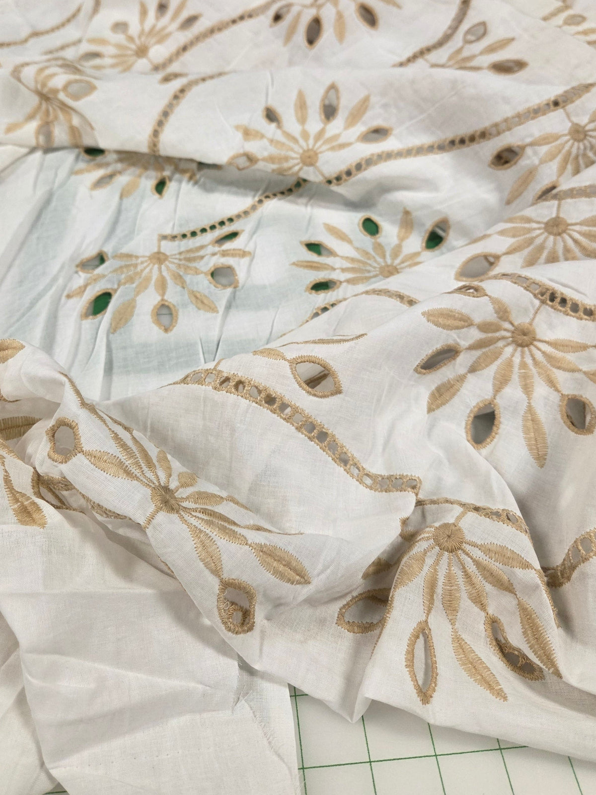 Close-up of white fabric with gold floral embroidery on a grid background