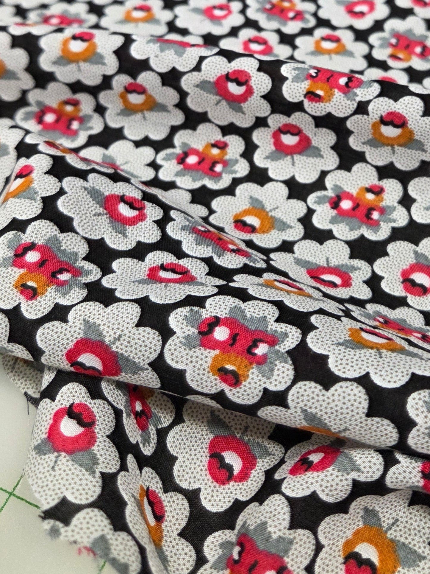 Floral fabric with small flowers on a black background, partially covering a white surface with green grid lines.