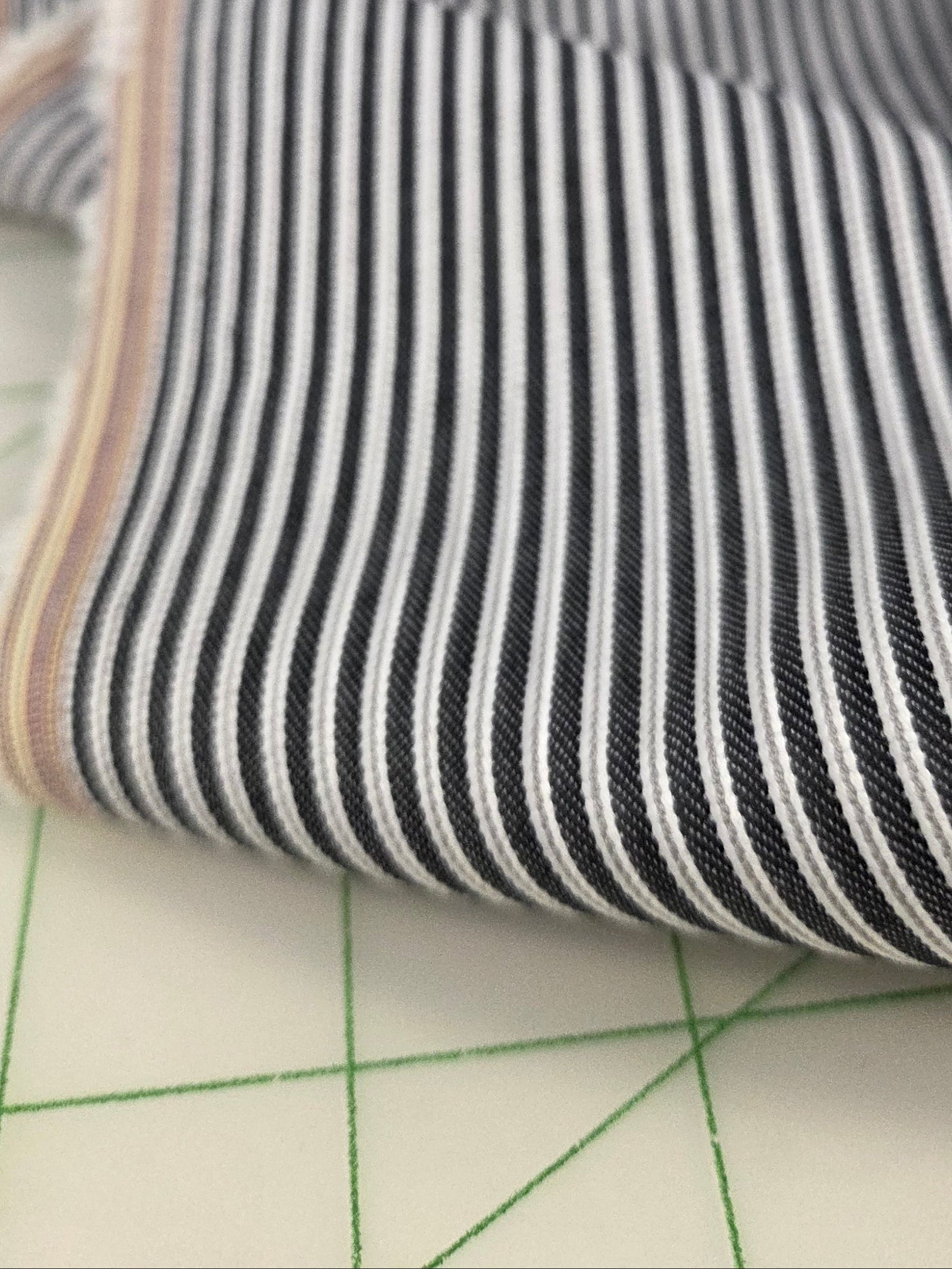 Close-up of striped fabric on a cutting mat o see colors of stripe is gray and white on indigo blue ground