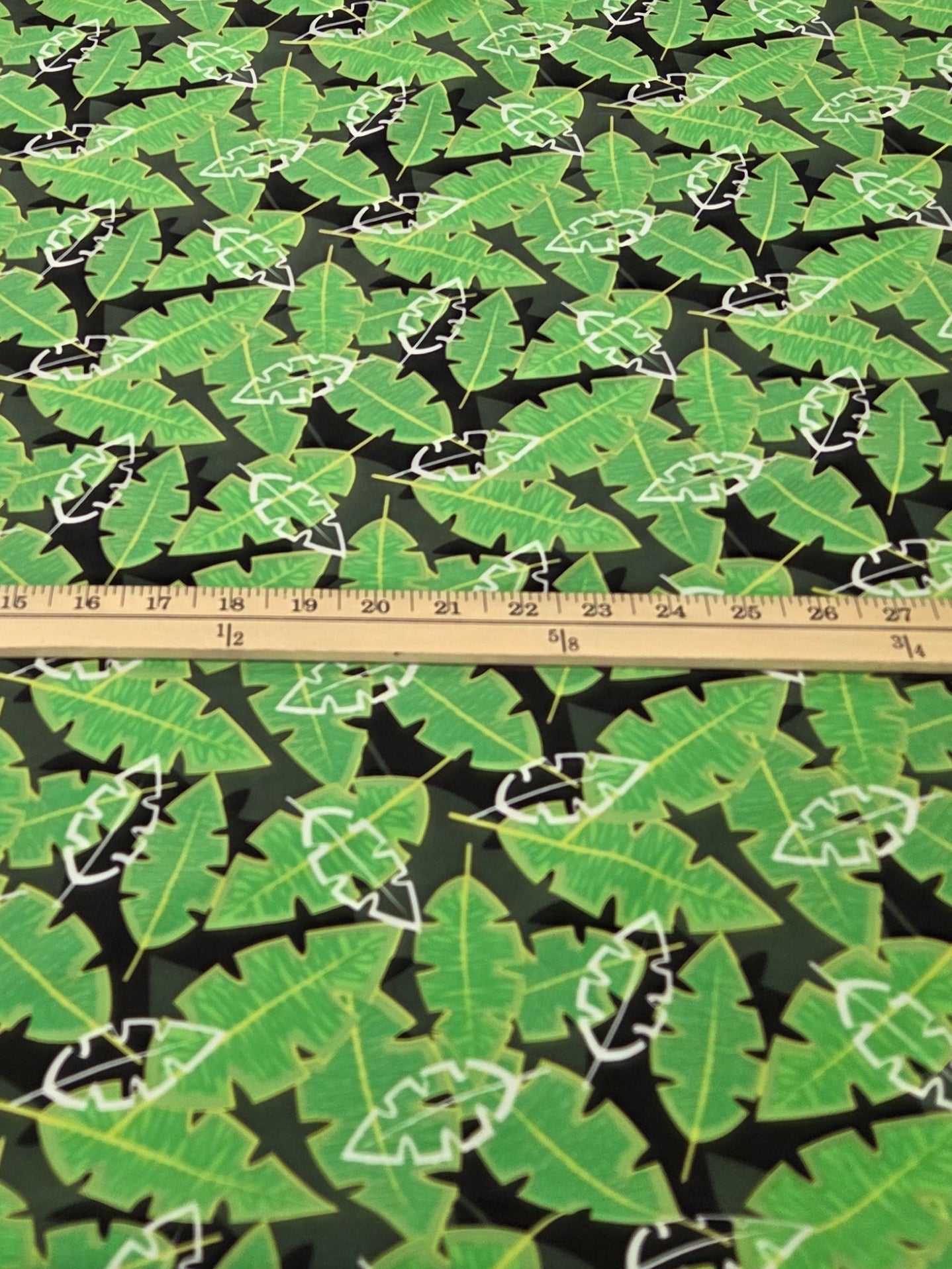Wall with green leaf pattern and a measuring tape, with clothing items in the background.