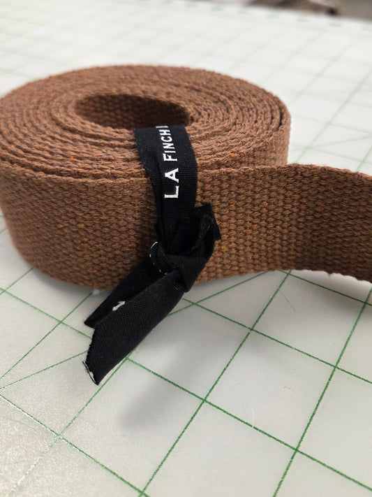 Brown woven belt with a black label on a white surface with green grid lines
