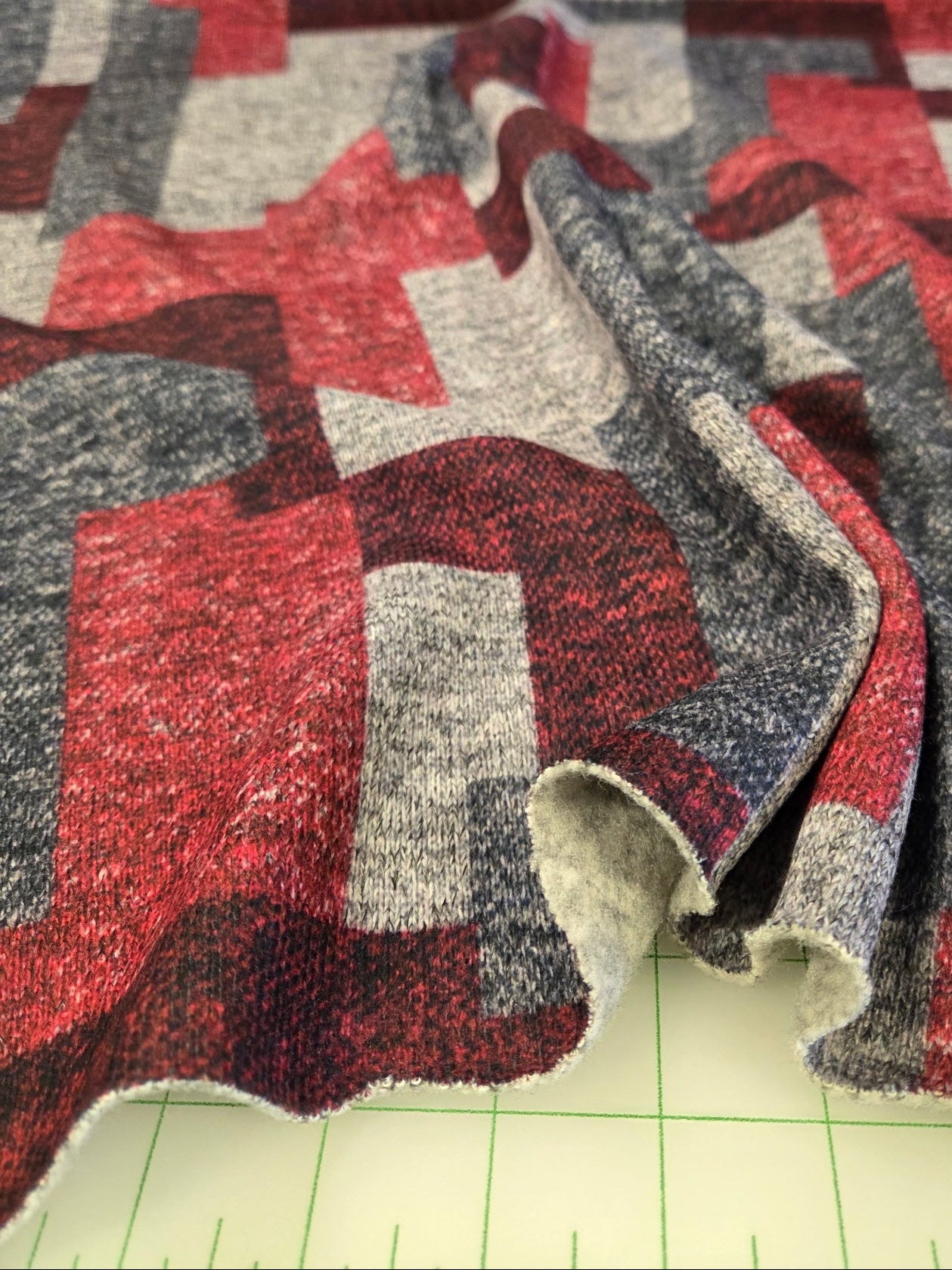 Textured fabric with red and gray pattern on a green cutting mat