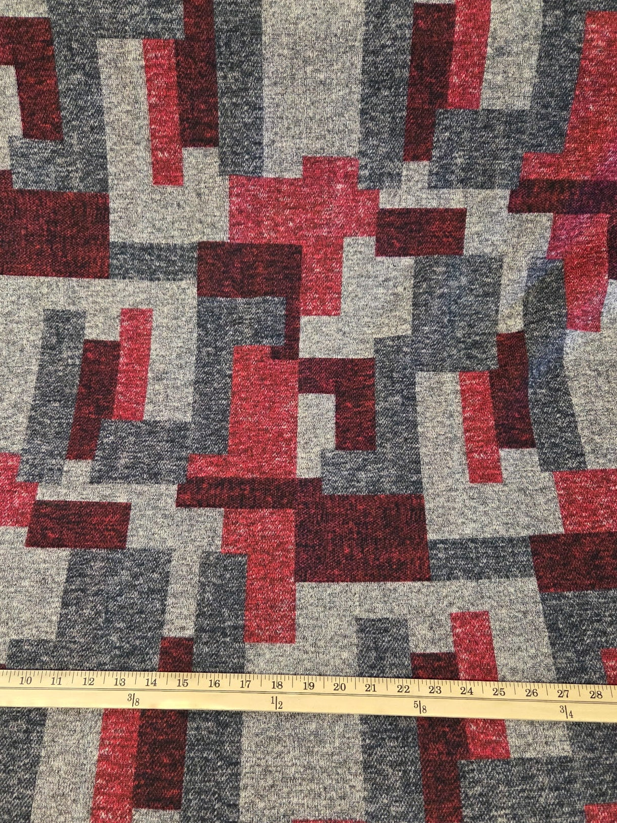 Geometric patterned fabric with red and gray colors, measured by a tape measure.