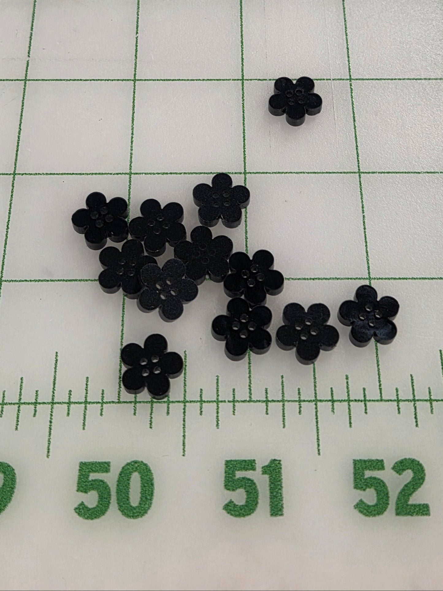 Small black flower-shaped objects on a white surface with green grid lines and measurements.
