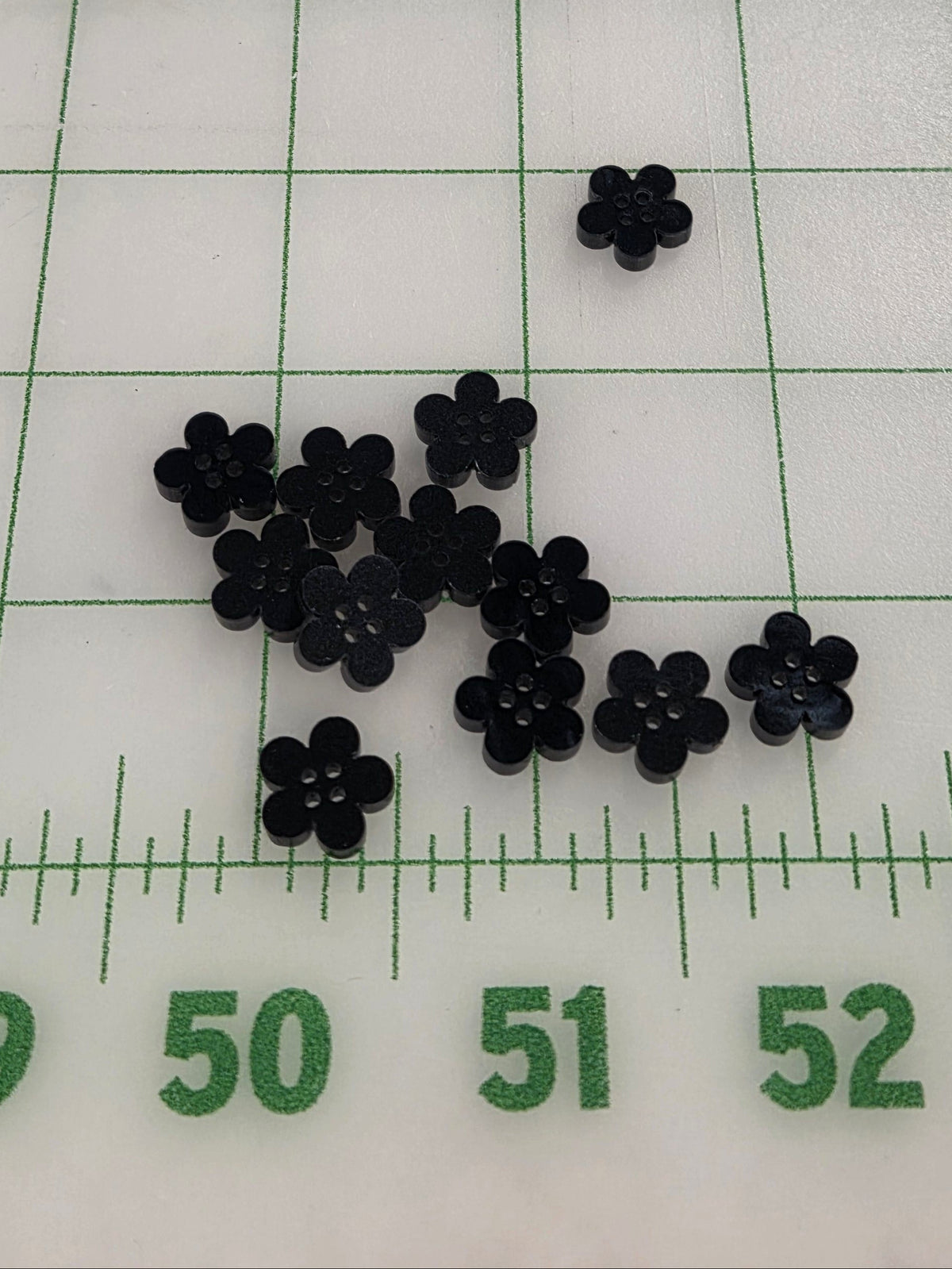 Small black flower-shaped objects on a white surface with green grid lines and measurements.