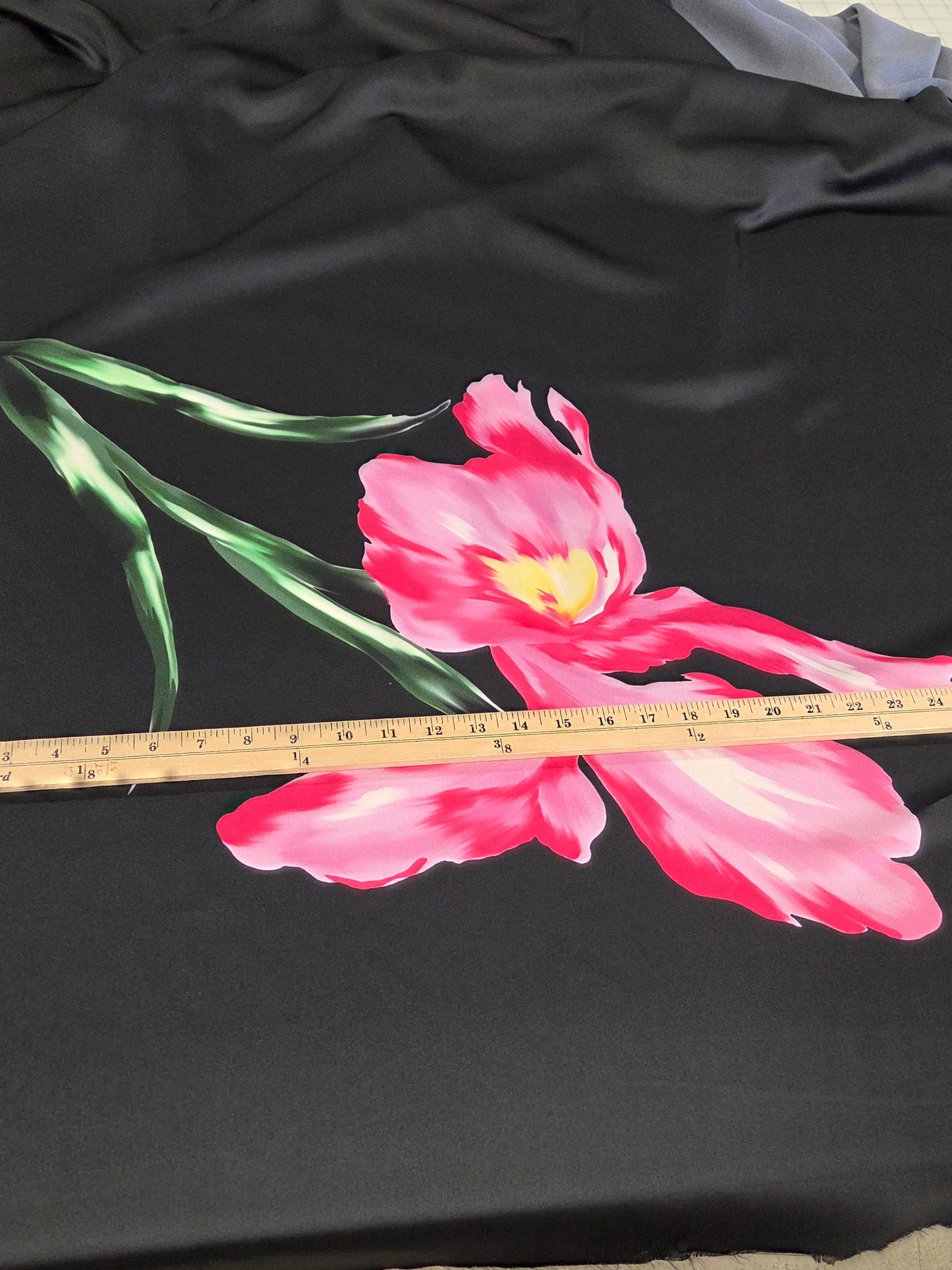 Black fabric with pink floral design and a ruler for scale on a neutral background