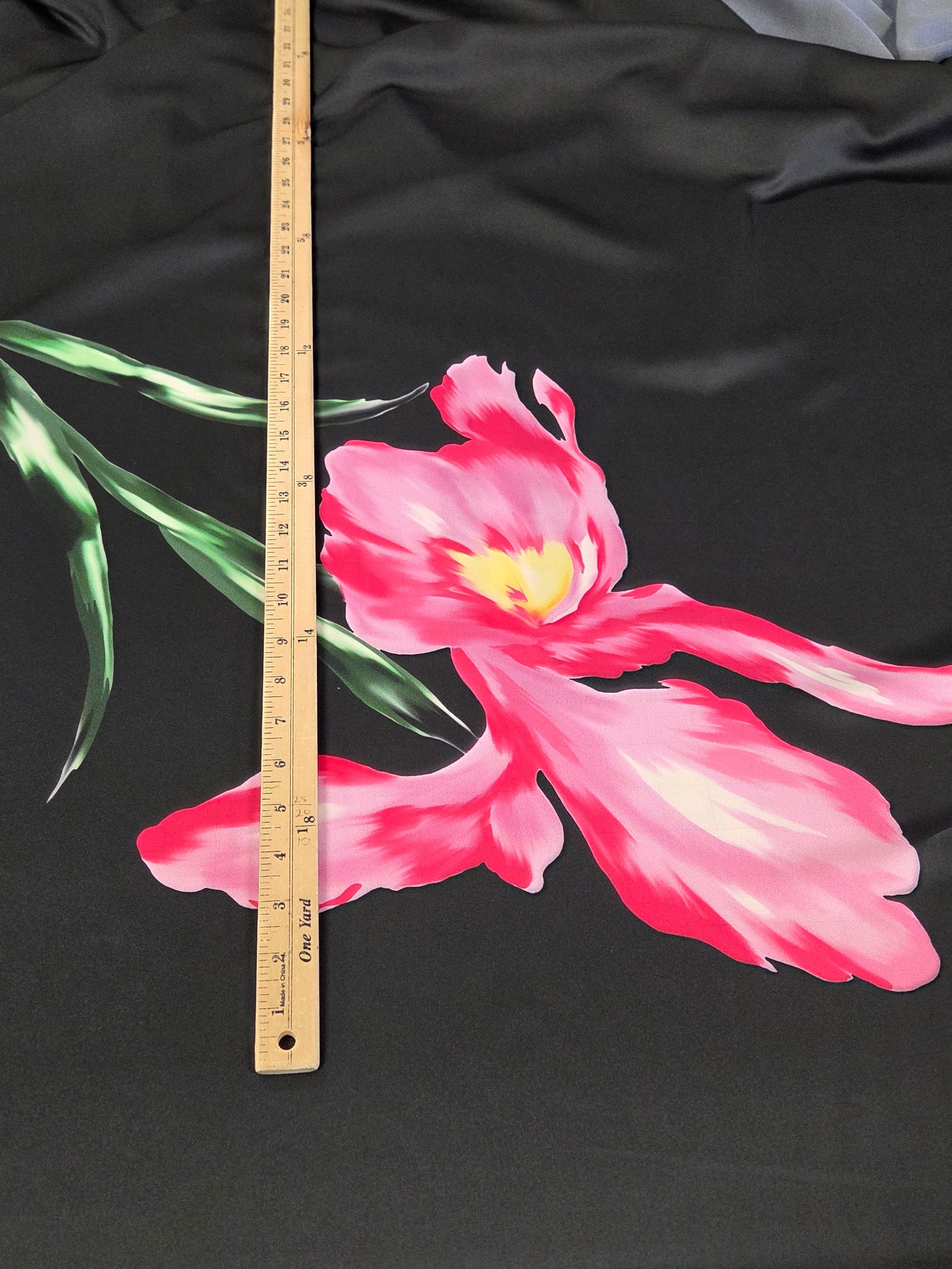 Black fabric with a pink flower design and a ruler for scale on a gray background