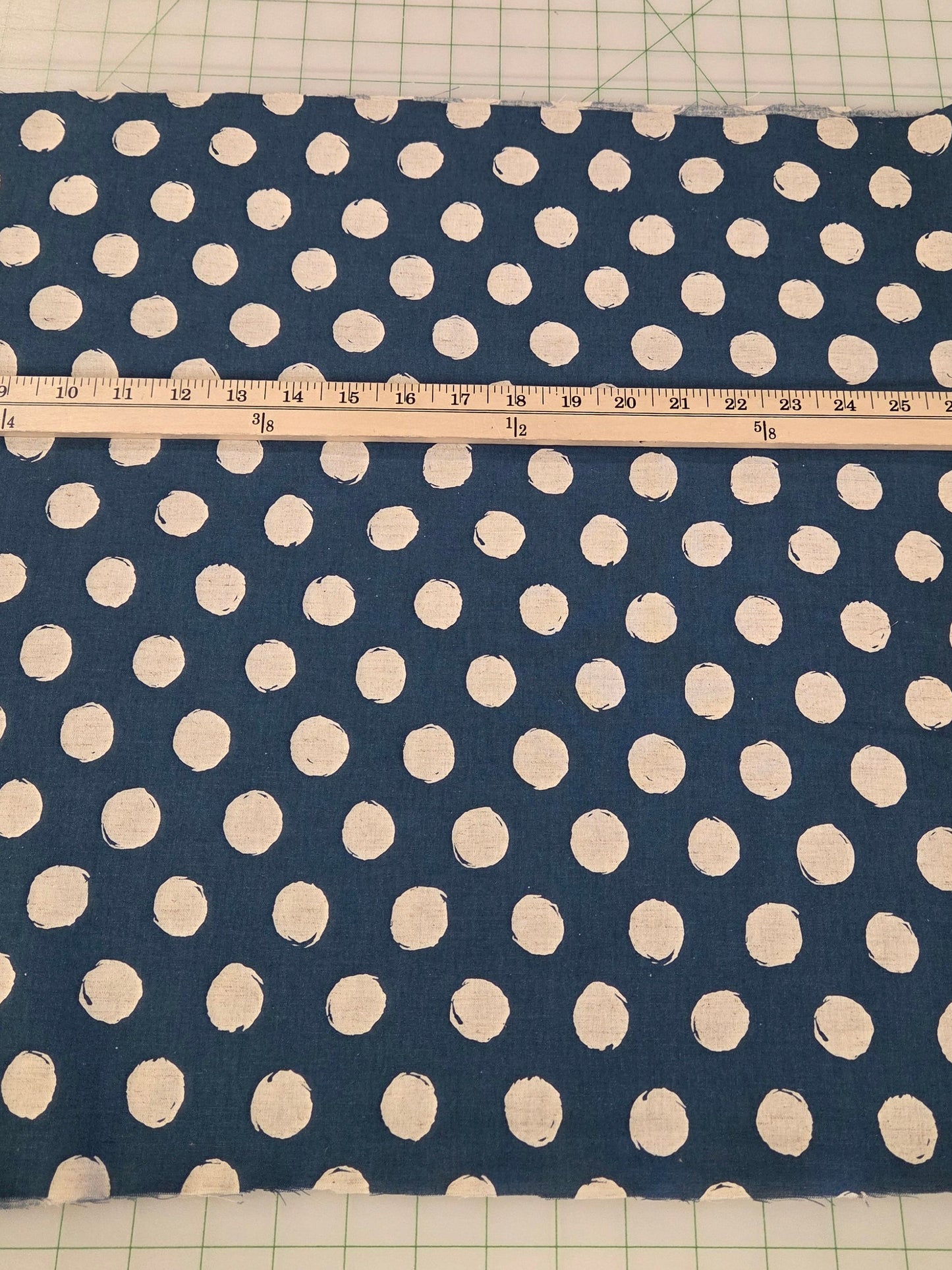 Navy blue fabric with white polka dots on a cutting mat with a ruler.