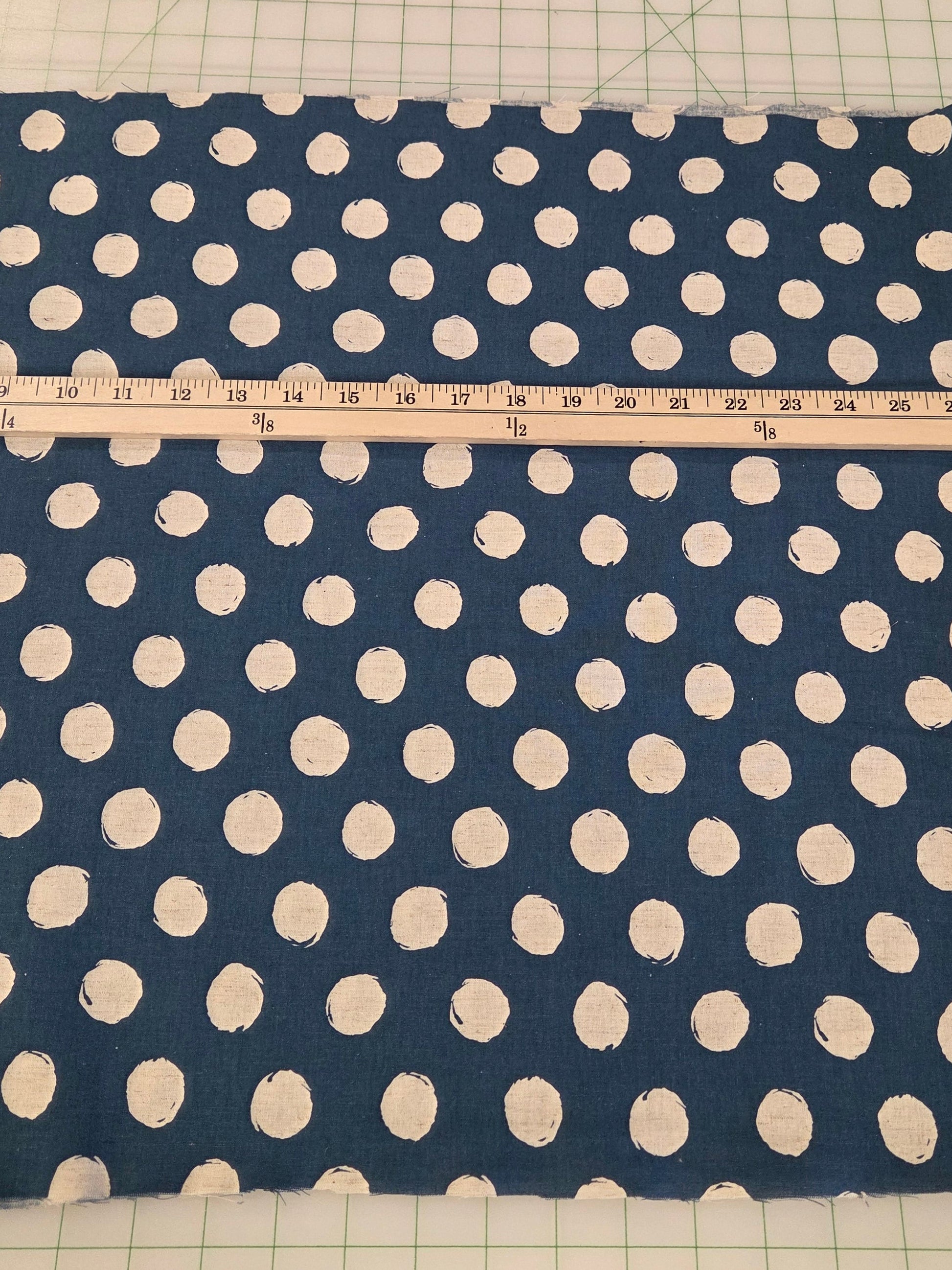 Navy blue fabric with white polka dots on a cutting mat with a ruler.