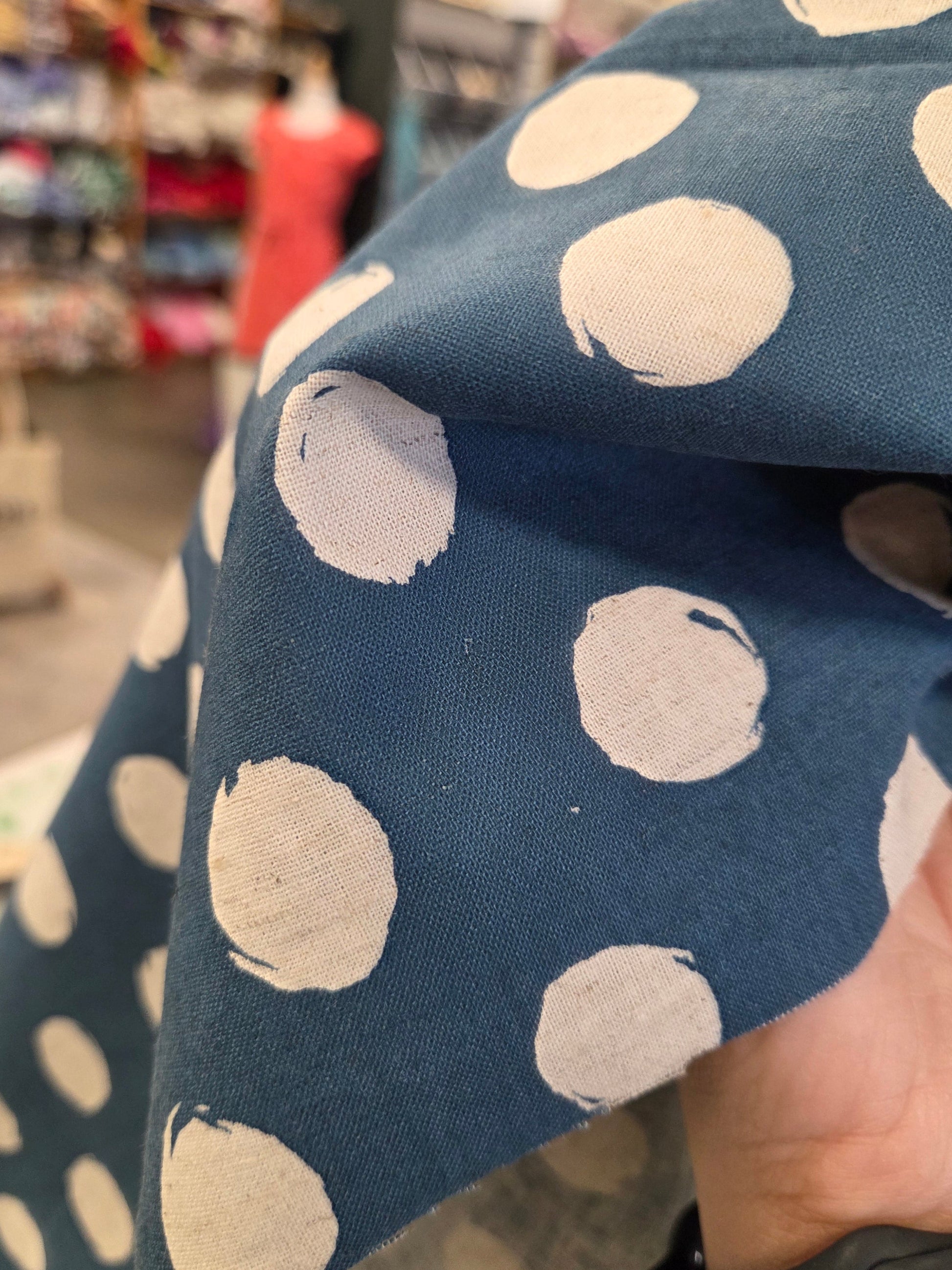Blue fabric with white polka dots held by a hand in an indoor setting