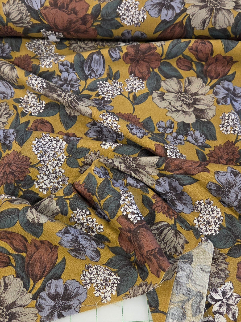 Floral fabric with brown and beige flowers on a yellow background, laid out on a cutting mat.