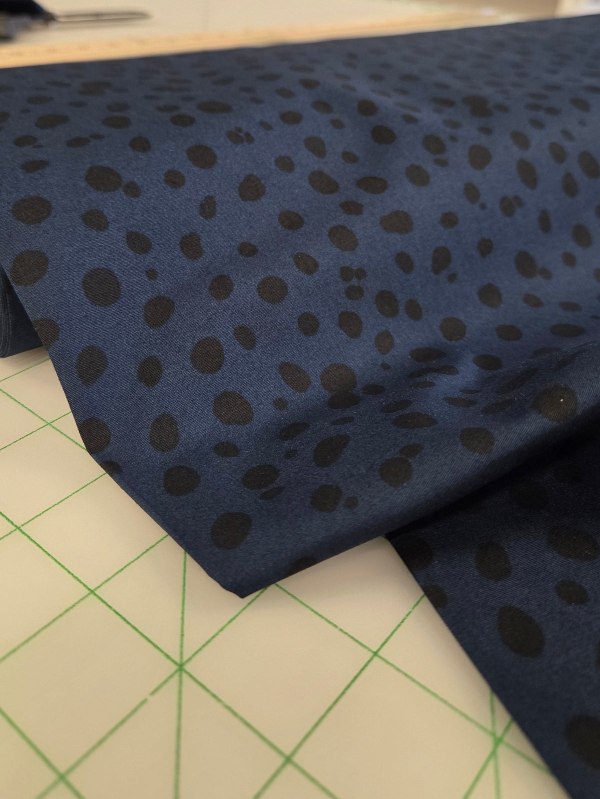 Roll of navy blue fabric with black polka dots on a grid surface, likely in a store or workshop setting.