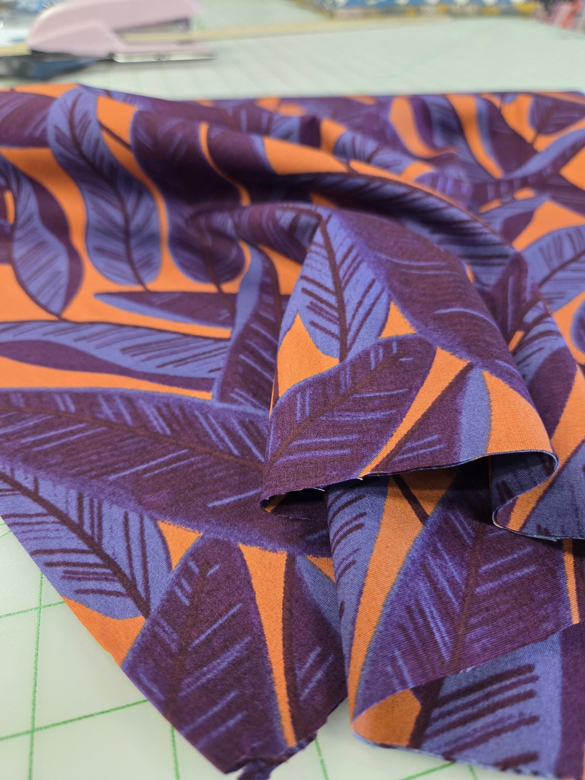 Roll of fabric with purple and orange leaf pattern on a cutting mat