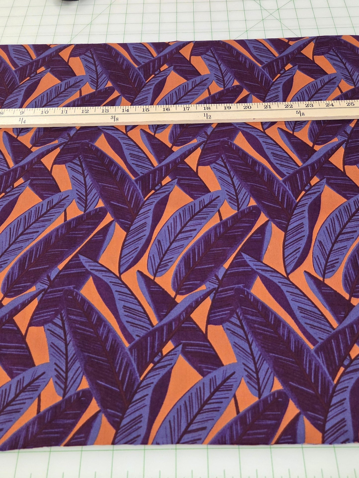 Fabric with purple and orange leaf pattern on a white grid background with measuring tape