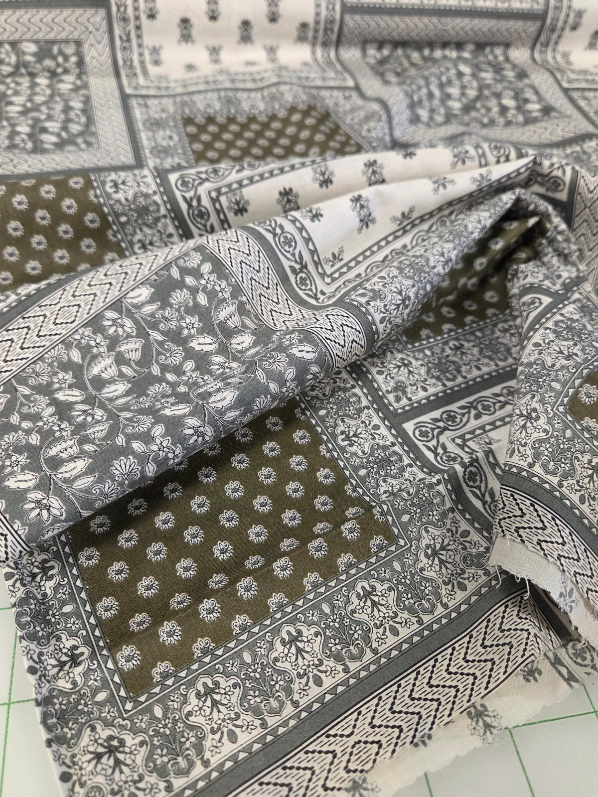 Patterned fabric with geometric and floral designs on a green grid background