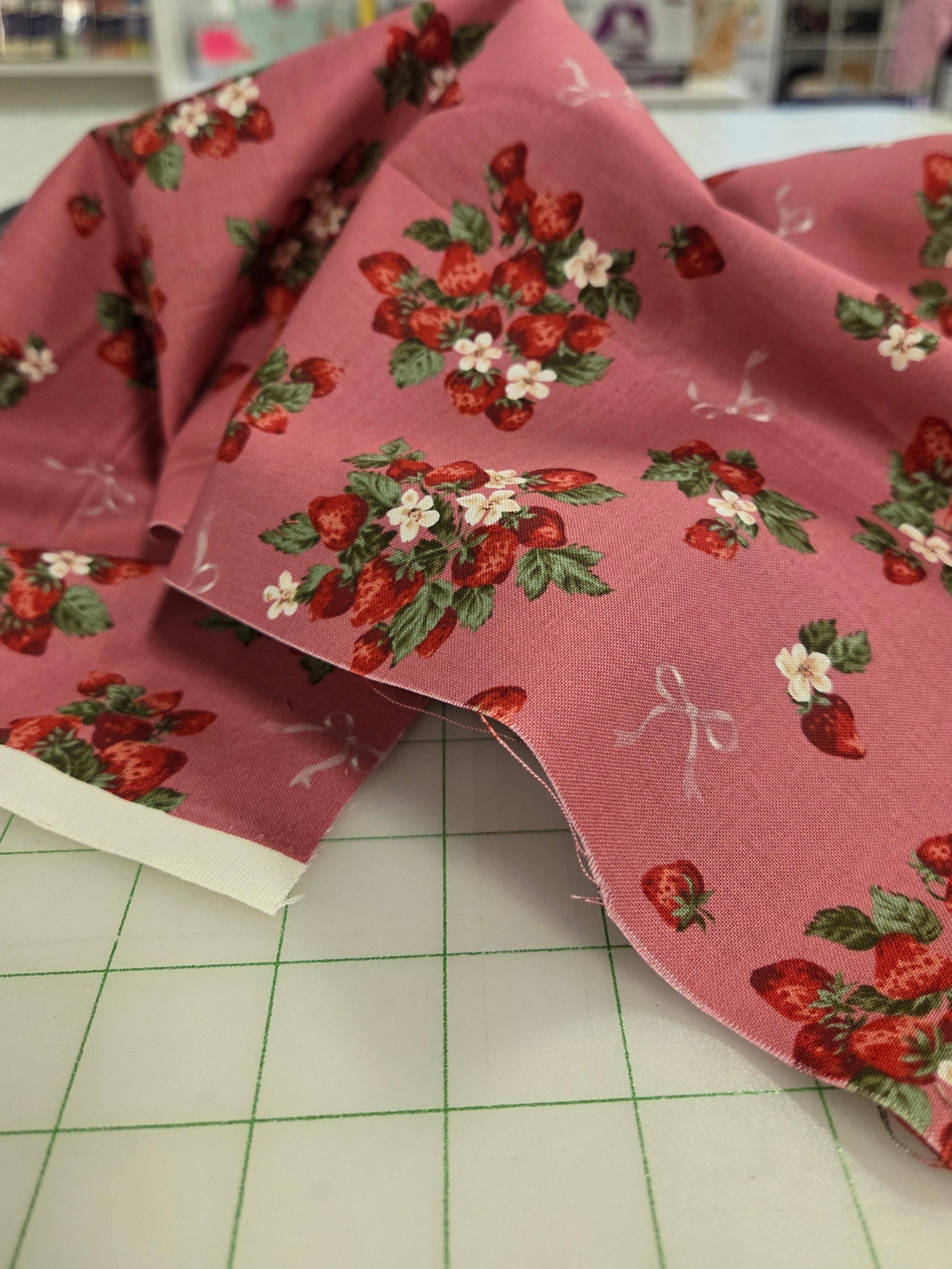 Fabric with strawberry pattern on a cutting mat in a store setting. UN No japan fabric 
