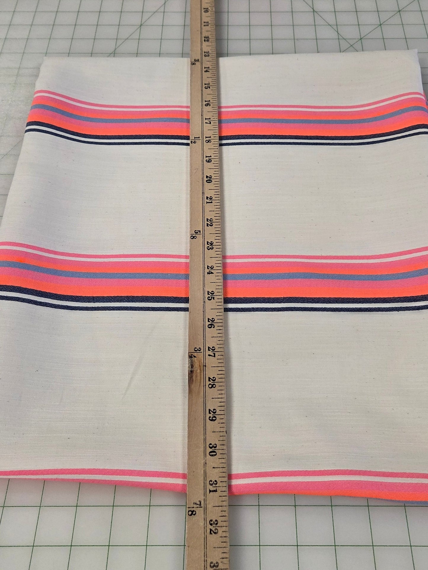 Fabric with pink and blue stripes on a grid surface, measured by a ruler.