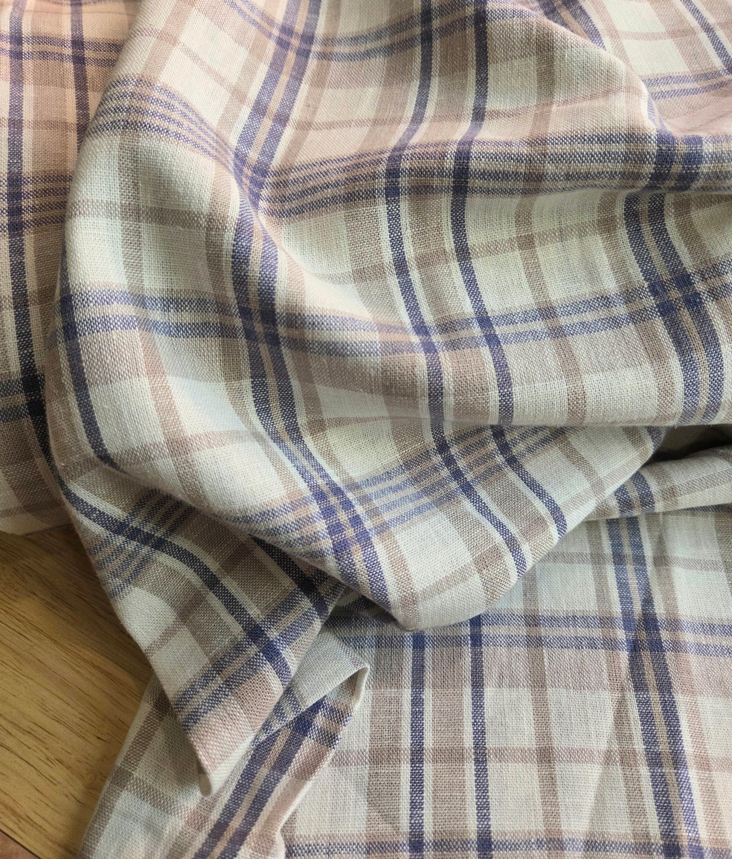Plaid fabric with brown and blue pattern on a wooden surface. Designer deadstock fabric by the yard. 