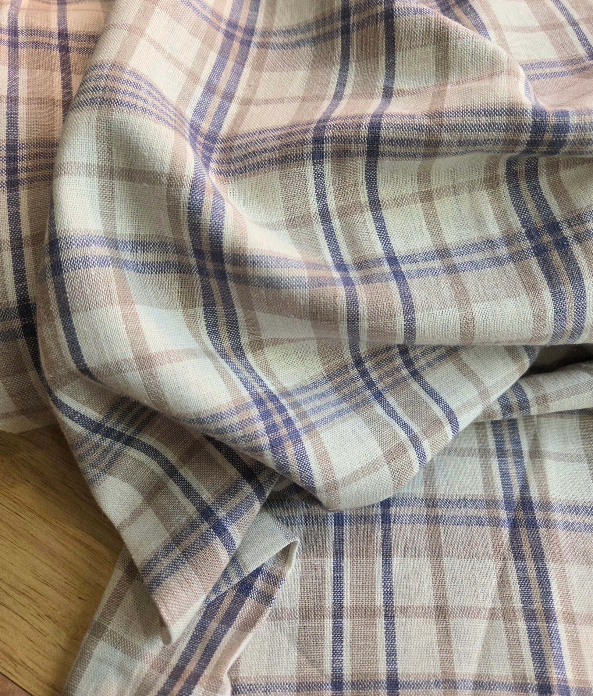 Plaid fabric with brown and blue pattern on a wooden surface. Designer deadstock fabric by the yard. 