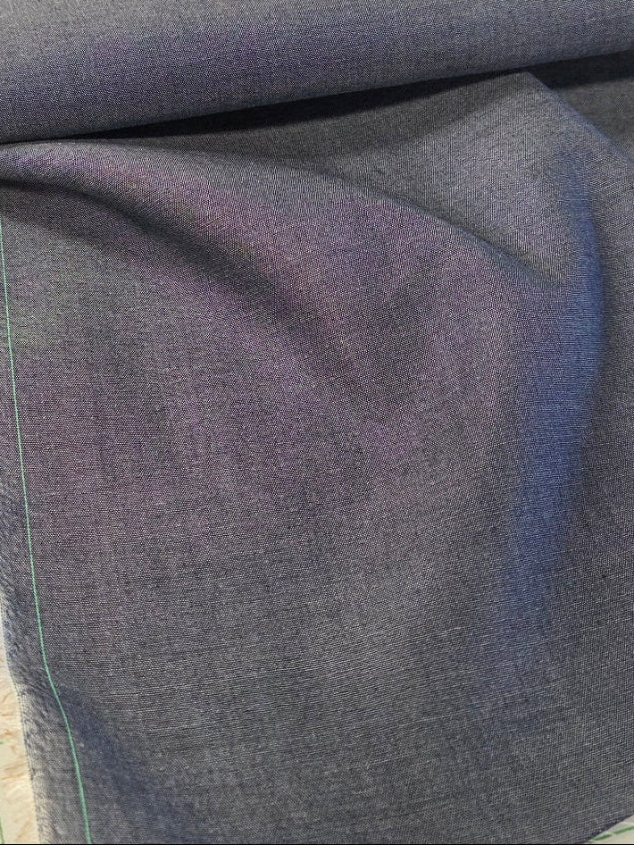 A close-up of folded blue-gray fabric, likely denim or chambray, laid on a white cutting mat with green grid lines.