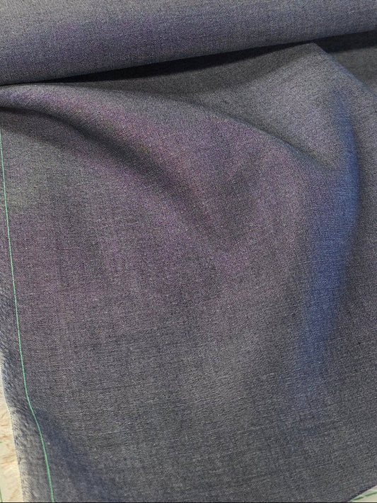 A close-up of folded blue-gray fabric, likely denim or chambray, laid on a white cutting mat with green grid lines.