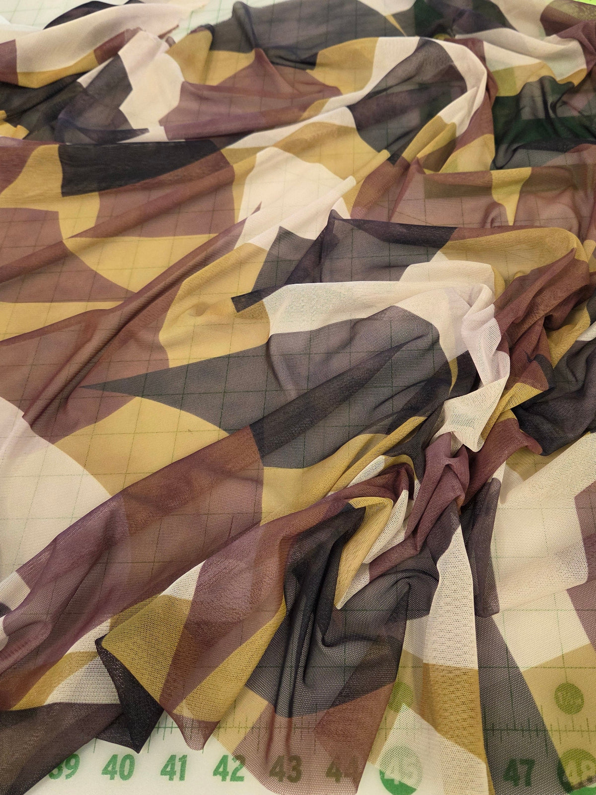 A sheer geometric patterned scarf or fabric draped over a measuring tape, showing a mix of brown, beige, white, and dark gray shapes.