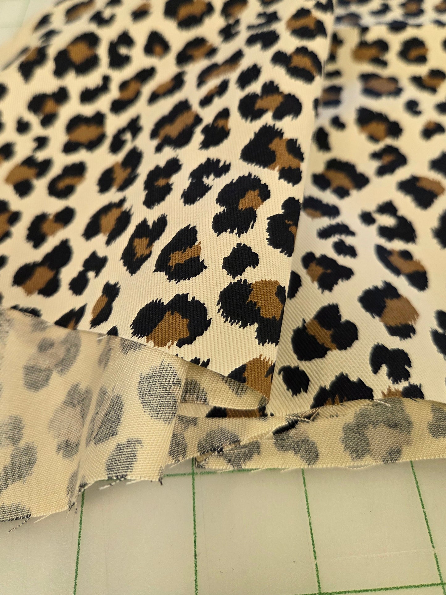 Leopard print fabric with black, brown, and beige spots, shown folded on a green-grid cutting mat.