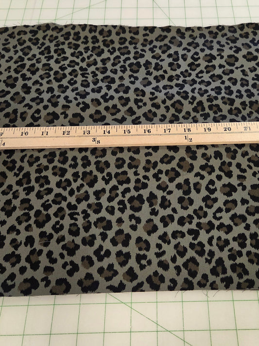 A rectangular piece of leopard print fabric laid flat on a green grid cutting mat, with a wooden ruler placed across the center to show the material width.
