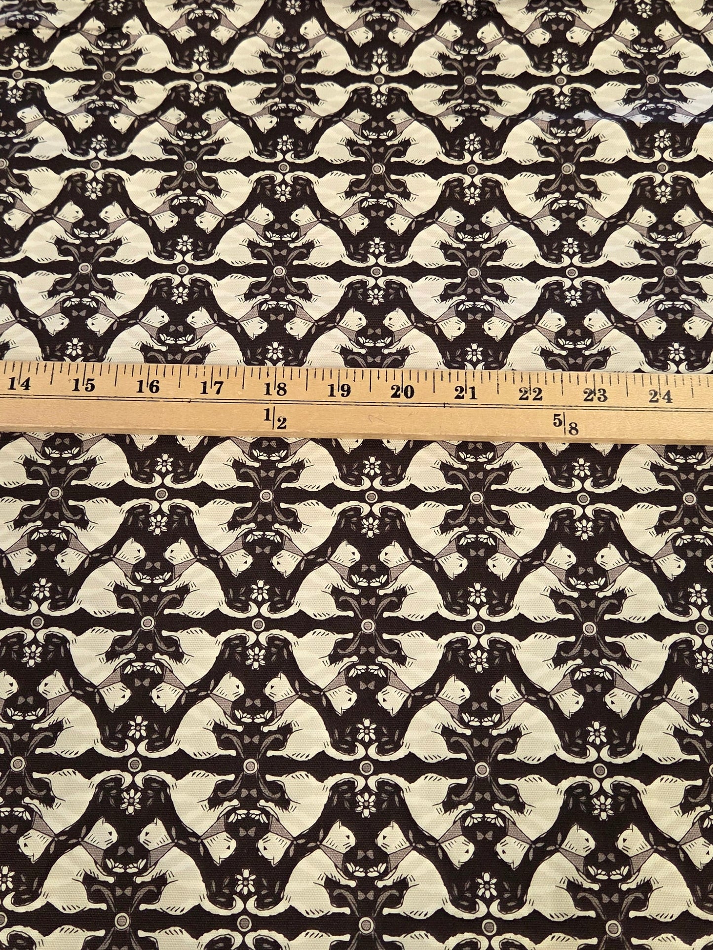 A rectangular piece of fabric with a black and white repeating ornamental damask pattern, laid flat on a green gridded cutting mat with a wooden ruler placed vertically down the center for scale.