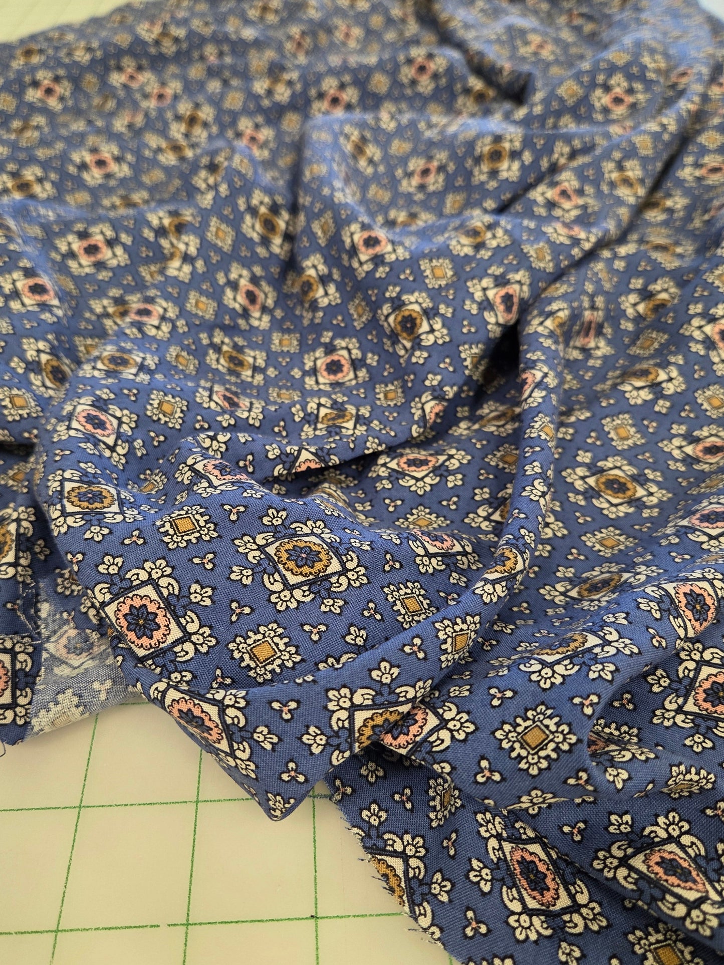 Blue patterned fabric with a small geometric and floral print, draped on a green grid cutting mat.