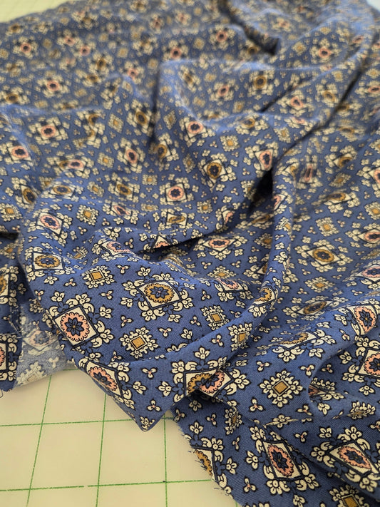 Blue patterned fabric with a small geometric and floral print, draped on a green grid cutting mat.