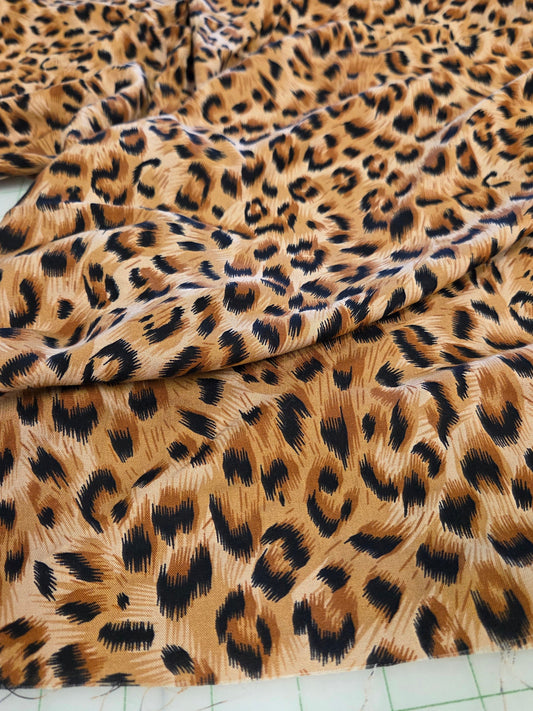Leopard print fabric draped on a white cutting mat, showing a classic animal spot pattern in brown, black, and beige tones.