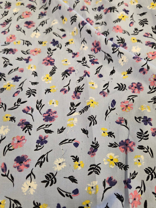 A close-up of a light gray fabric with an all-over small floral print in pink, yellow, purple, and white, with black leafy stems.