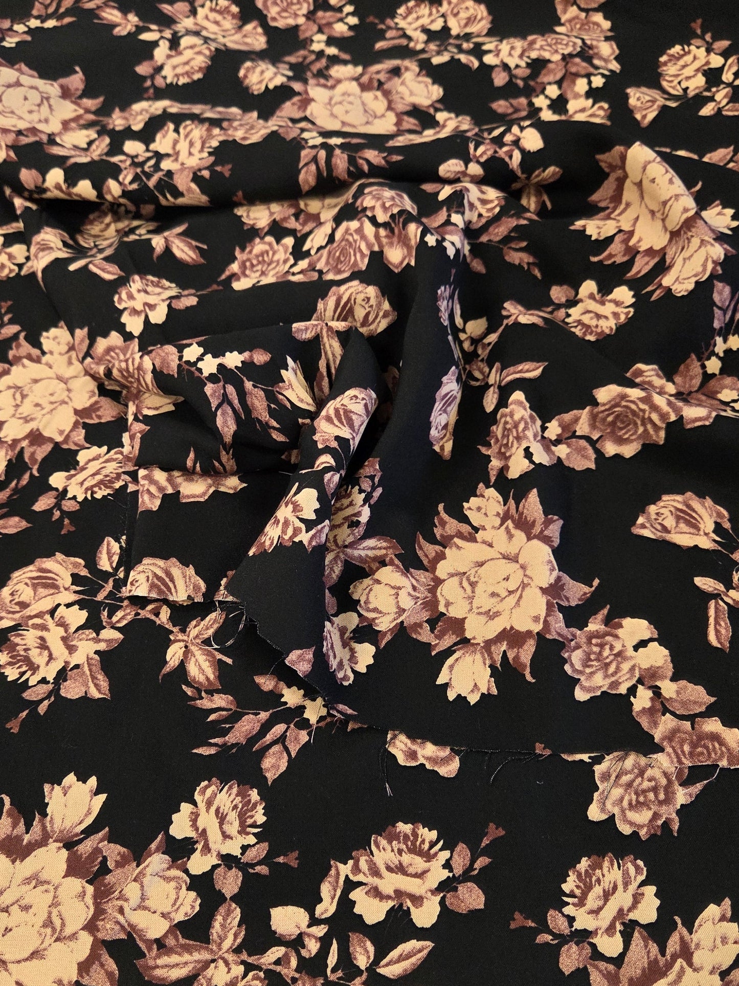 A piece of black fabric with a vintage floral pattern in dusty pink and beige, laid flat on a green gridded cutting mat.