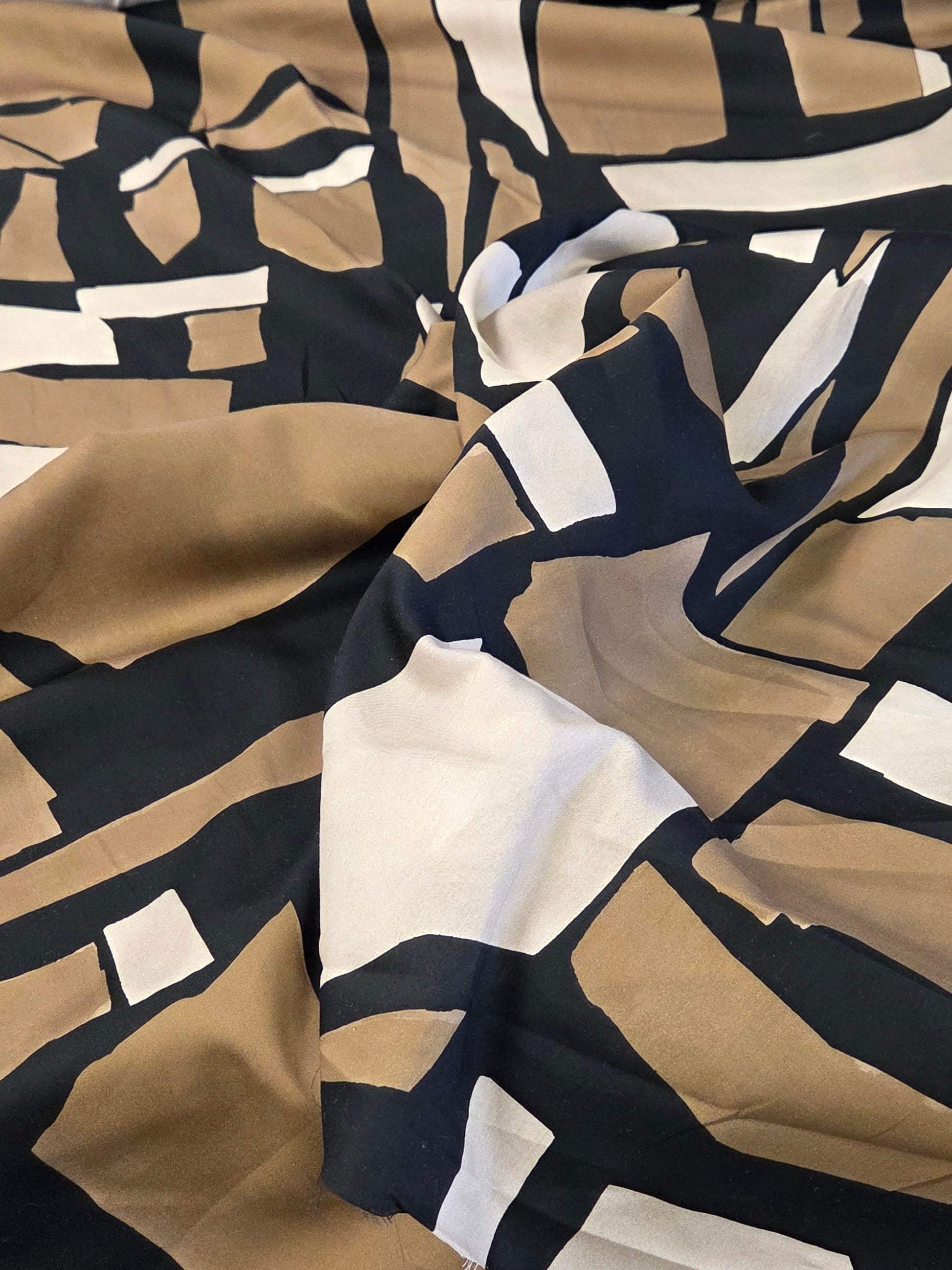 A close-up of draped fabric with an abstract geometric pattern in beige, black, and white, with a matching rolled fabric visible on the left.