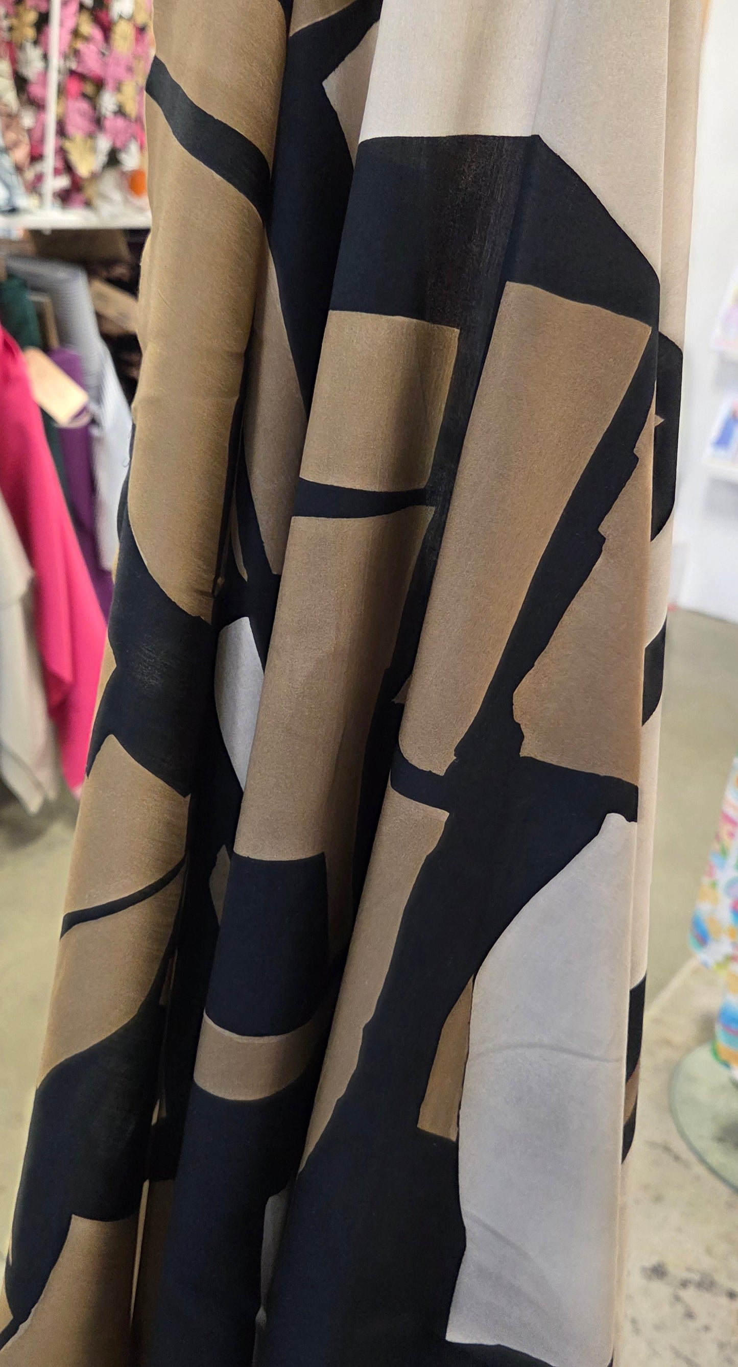 A close-up of a folded fabric or wallpaper sample with an abstract geometric pattern in beige, black, and white, photographed in what appears to be a store or display area.