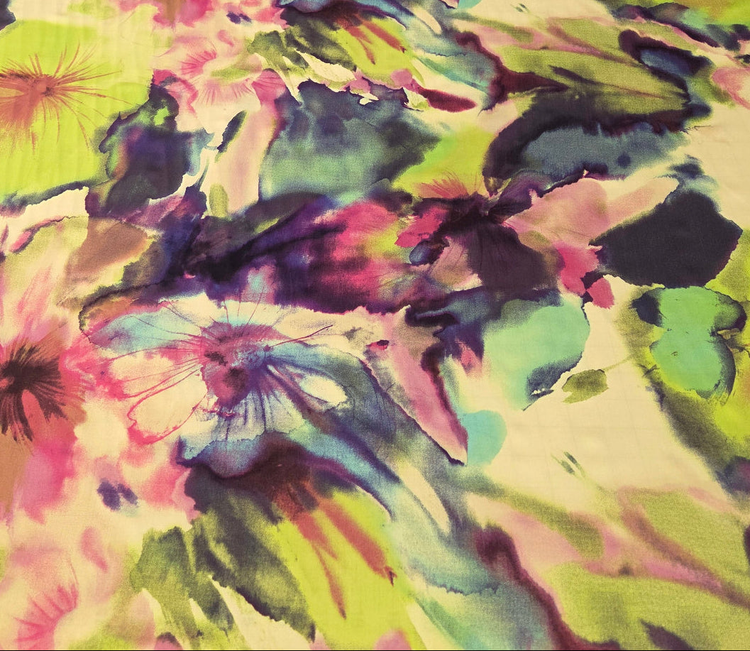A vibrant floral fabric with an abstract watercolor pattern in shades of lime green, pink, purple, and blue, draped over a rack next to other folded textiles.