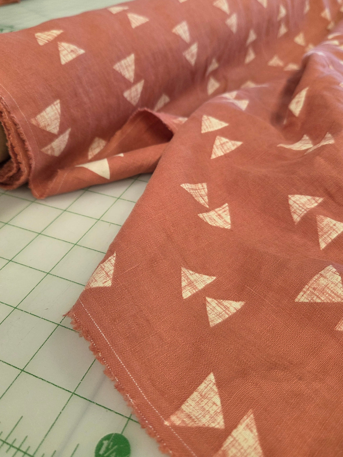A close-up of terracotta-colored fabric with a repeating white geometric triangle pattern, draped over a white gridded cutting mat.
