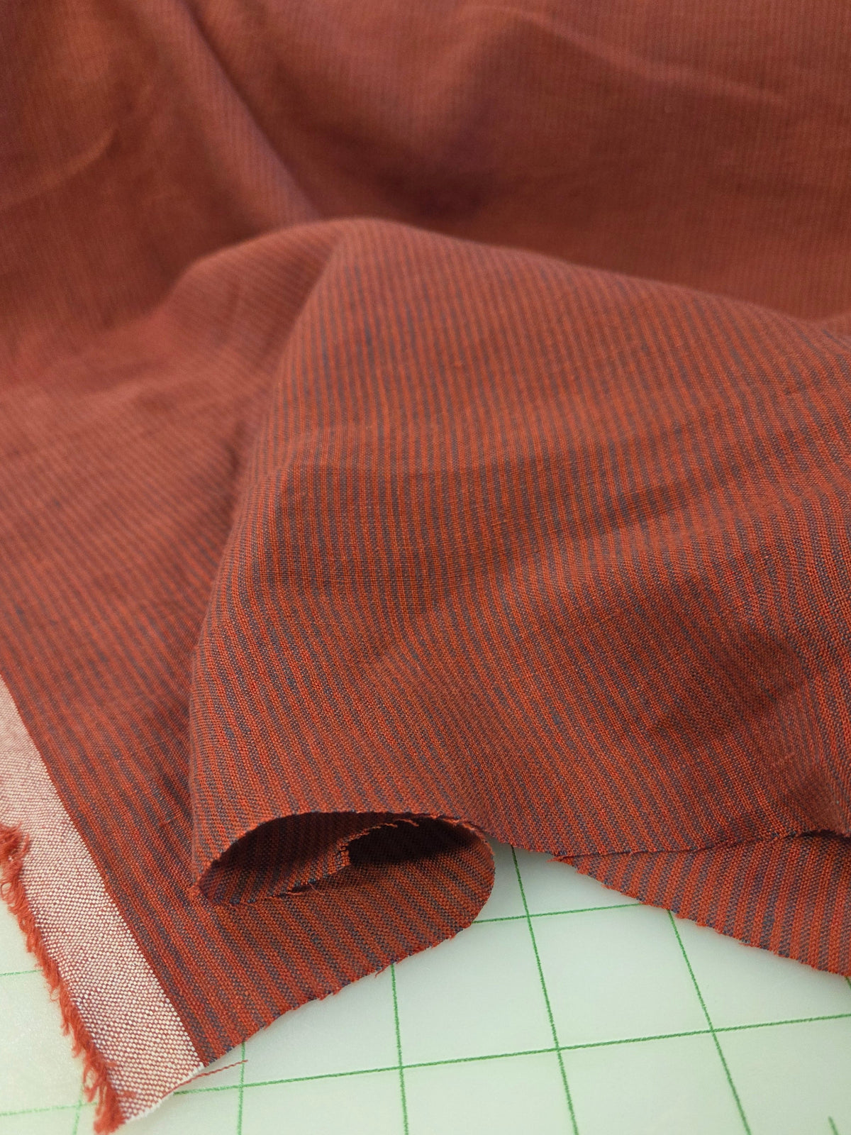 A close-up of rust-brown striped fabric draped over a white cutting mat with green grid lines.