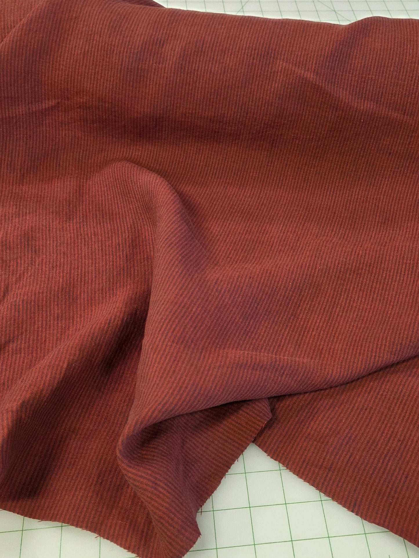 A piece of rust-colored ribbed fabric draped over a white cutting mat with green measurement markings.