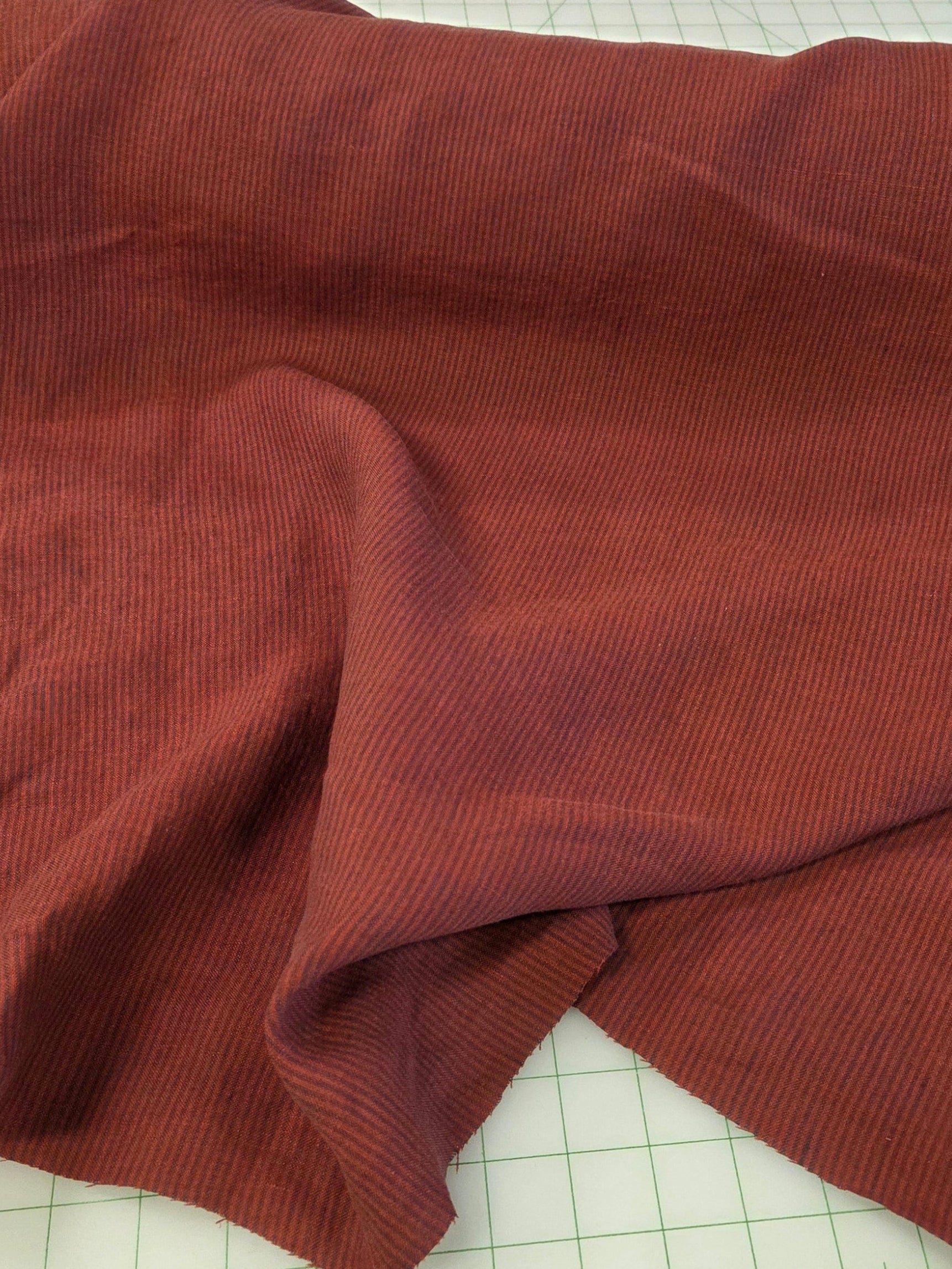 A piece of rust-colored ribbed fabric draped over a white cutting mat with green measurement markings.