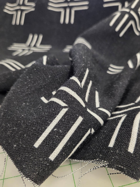 A close-up of a black woven fabric with a white geometric pattern, draped over a beige cutting mat with green grid lines.