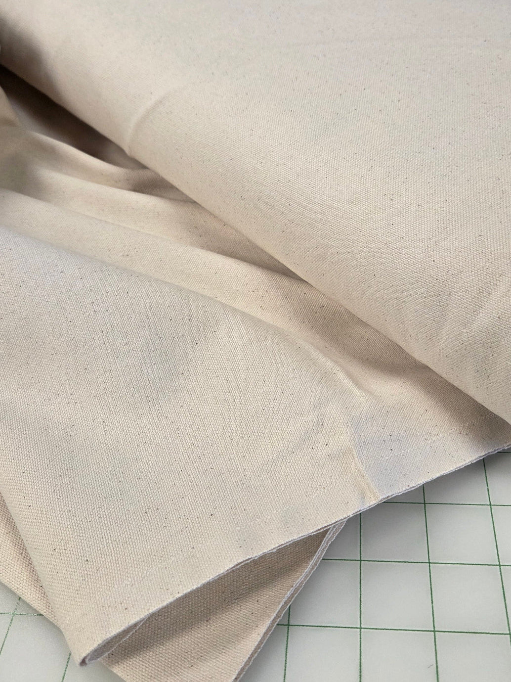 A close-up of a roll of off-white or cream canvas fabric draped over a gridded cutting mat.