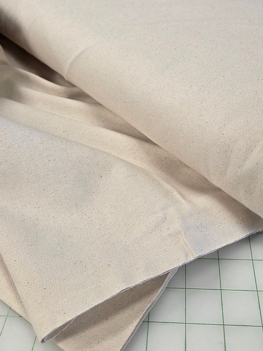 A close-up of a roll of off-white or cream canvas fabric draped over a gridded cutting mat.