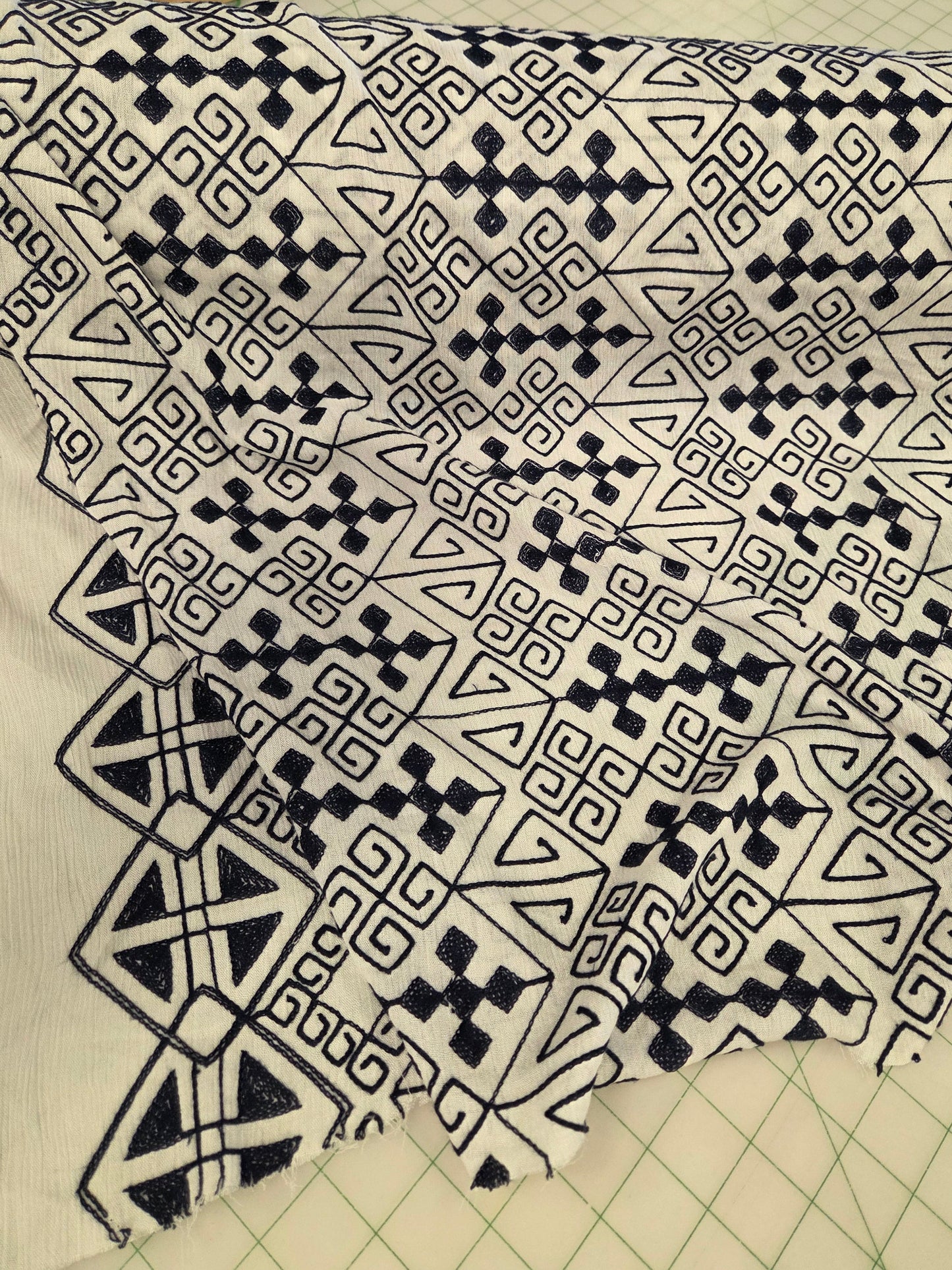 blue and white patterned fabric draped over a cutting mat, featuring a geometric tribal-style print with triangles, diamonds, and zigzags.