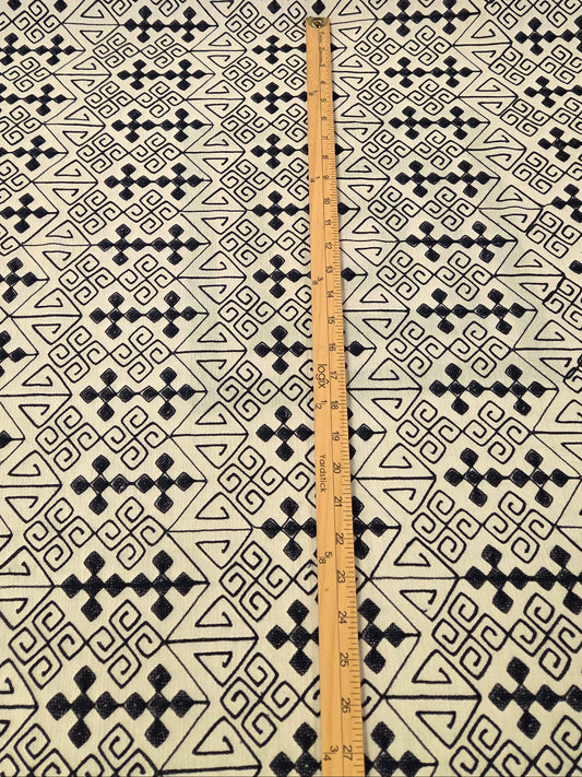 A close-up of a blue geometric patterned fabric, with a wooden ruler placed vertically in the center to show the scale of the pattern.