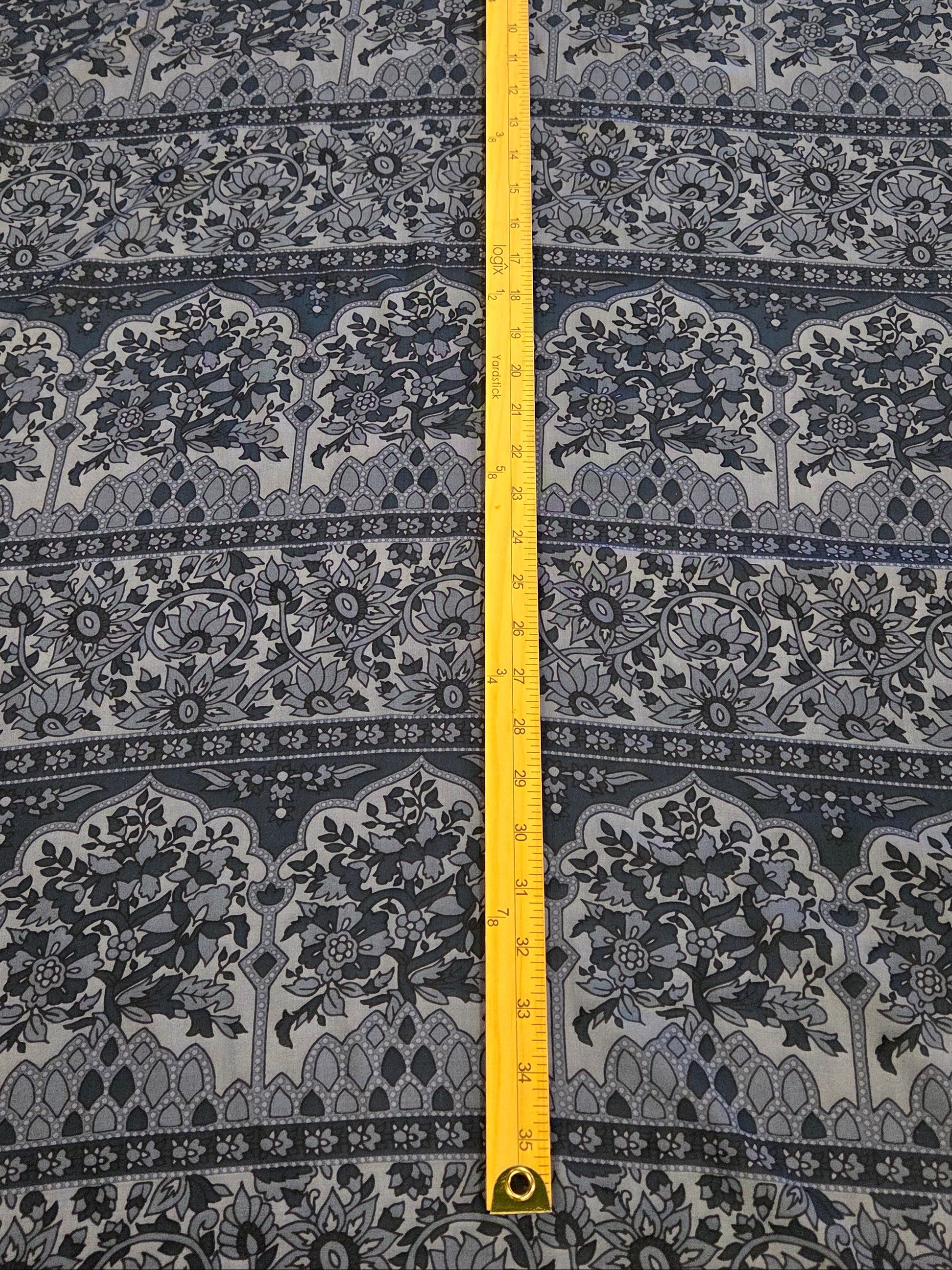 A navy blue and gray patterned fabric  on a cutting mat, with a yellow tape measure standing vertically in the center to show the height.