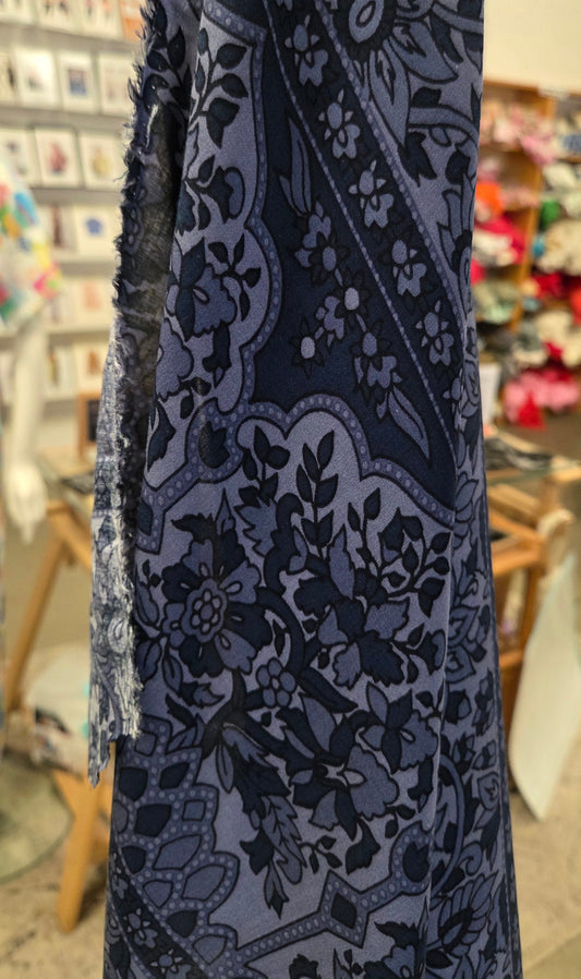 A close-up of a dark blue and gray patterned fabric draped over a mannequin in a clothing store. The fabric features a detailed floral and paisley design with a frayed edge.