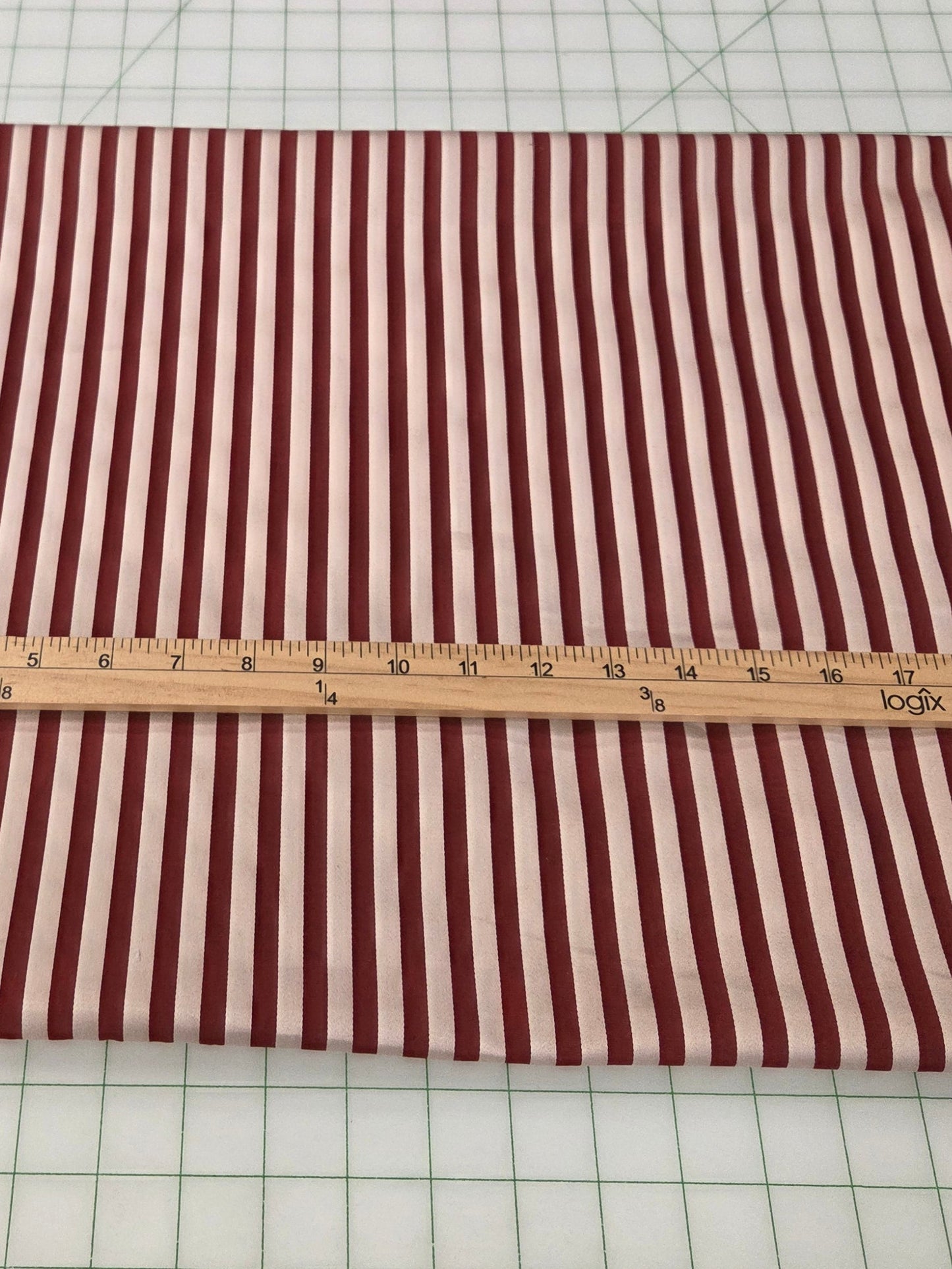 A rectangular piece of fabric with vertical red and white stripes is laid flat on a white gridded cutting mat, with a wooden ruler placed horizontally across the center for scale.