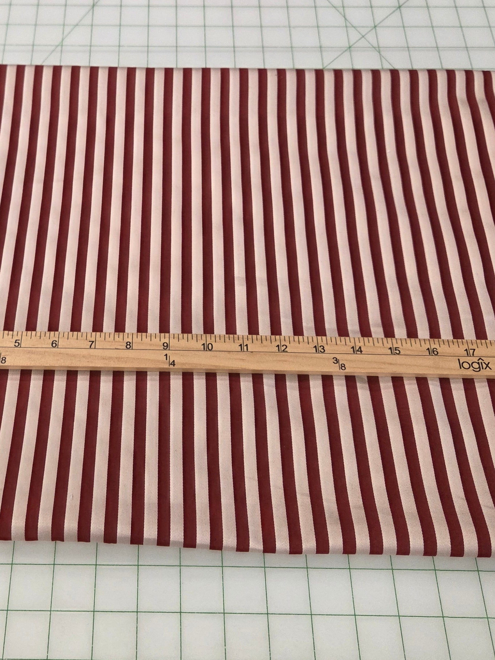 A rectangular piece of fabric with vertical red and white stripes is laid flat on a white gridded cutting mat, with a wooden ruler placed horizontally across the center for scale.